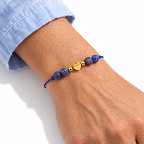Bracelet cœur doré et quatre sodalites porté sur un poignet incliné, manche bleu clair