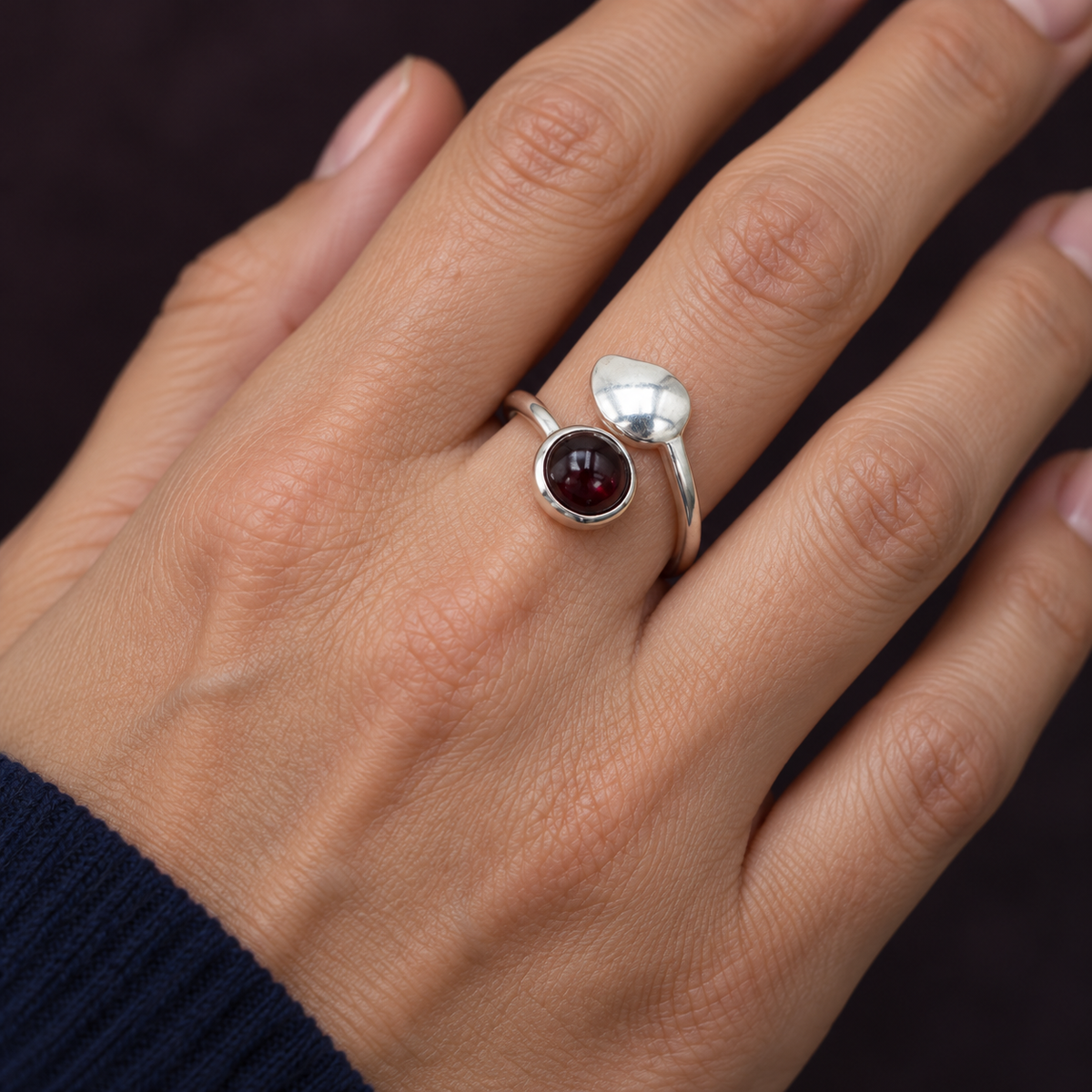Bague en argent et grenat rhodolite au doigt, main détendue près d’une manche bleu nuit