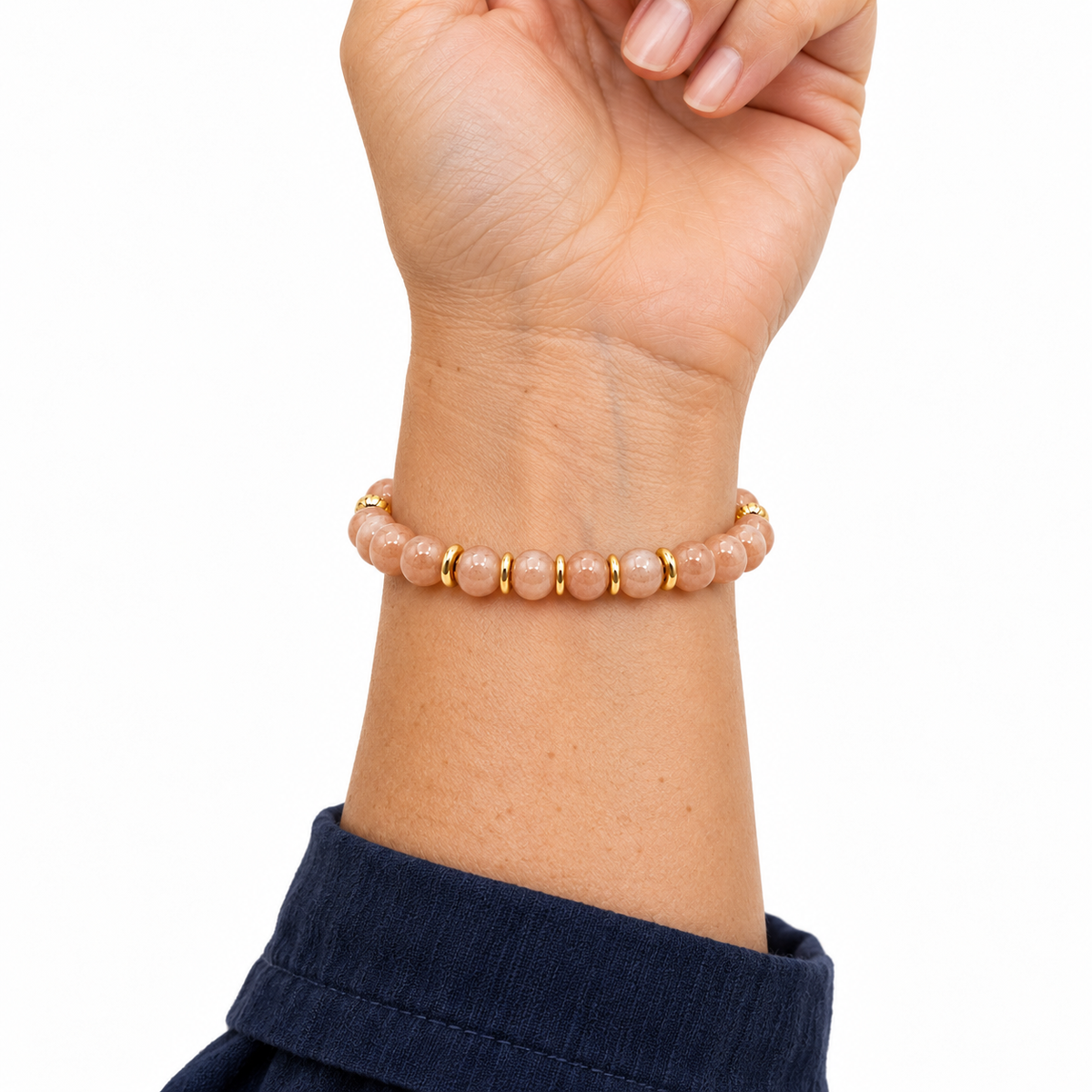 Bracelet doré en pierre de lune rose porté au poignet, main relevée sur fond blanc
