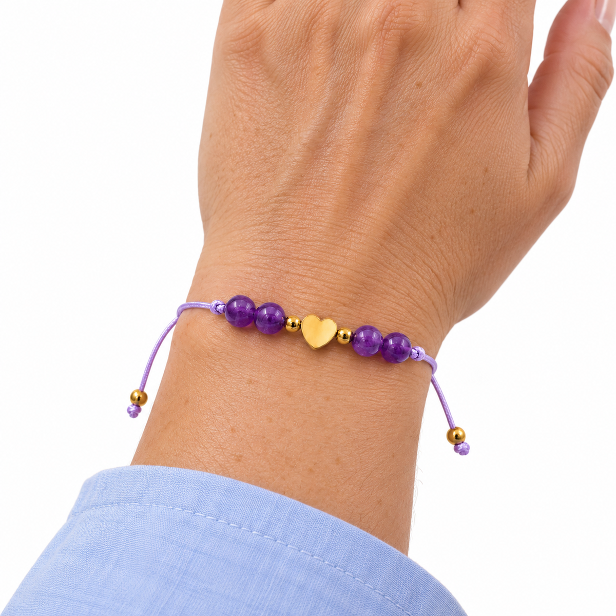 Bracelet cœur doré en améthyste porté au poignet, main relevée sur fond blanc