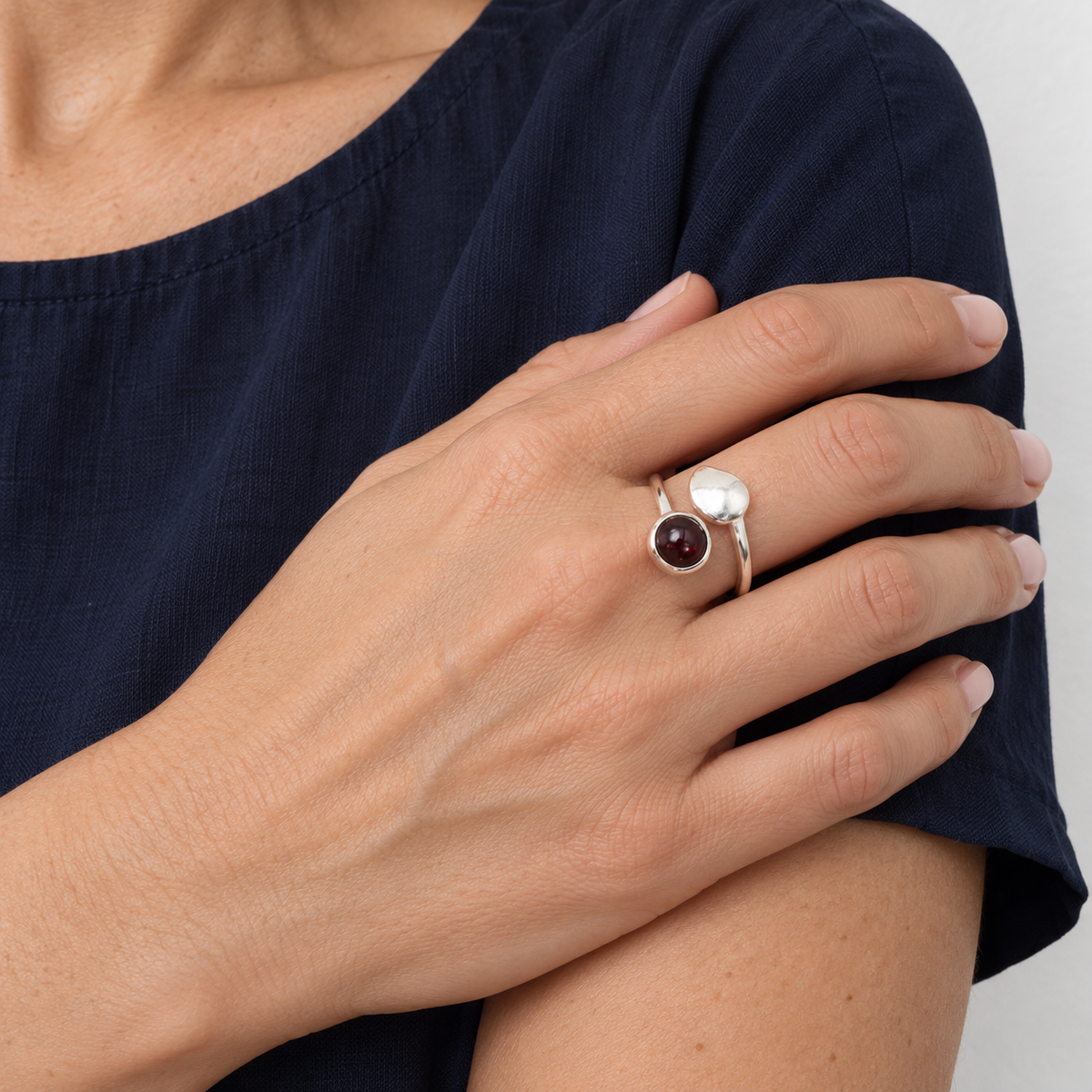 Bague au grenat rhodolite portée sur une main près du buste, blouse bleu nuit