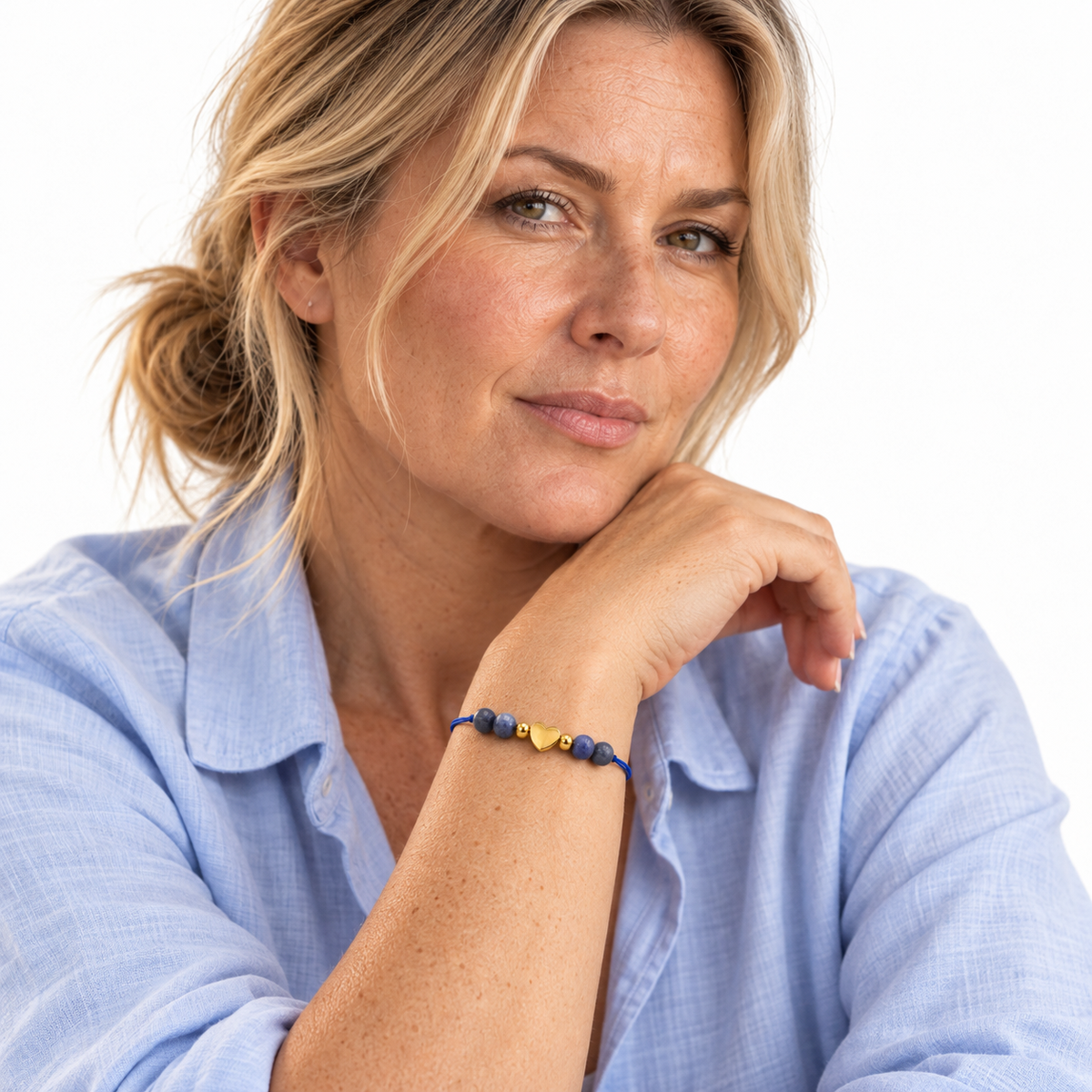 Bracelet cœur doré et sodalite porté avec une chemise bleu clair, poignet au premier plan