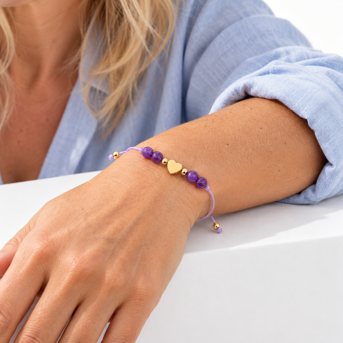 Bracelet cœur doré en améthyste porté, avant-bras posé sur une surface blanche
