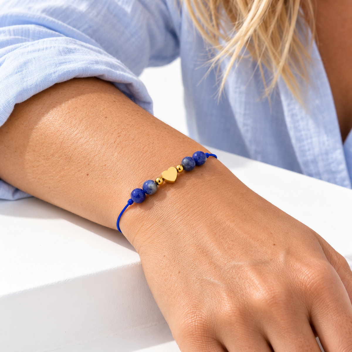 Bracelet cœur doré en sodalite porté, avant-bras posé sur une surface blanche