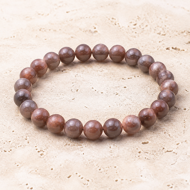 Bracelet en pierre de soleil noire orangée 10 mm - 16 à 18 cm, vue complète sur une surface minérale claire