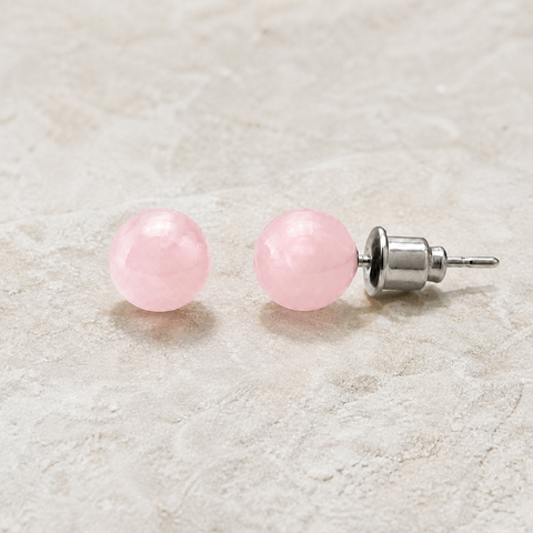 Boucles d'oreilles puces en quartz rose 6 mm, vue complète sur une surface minérale claire