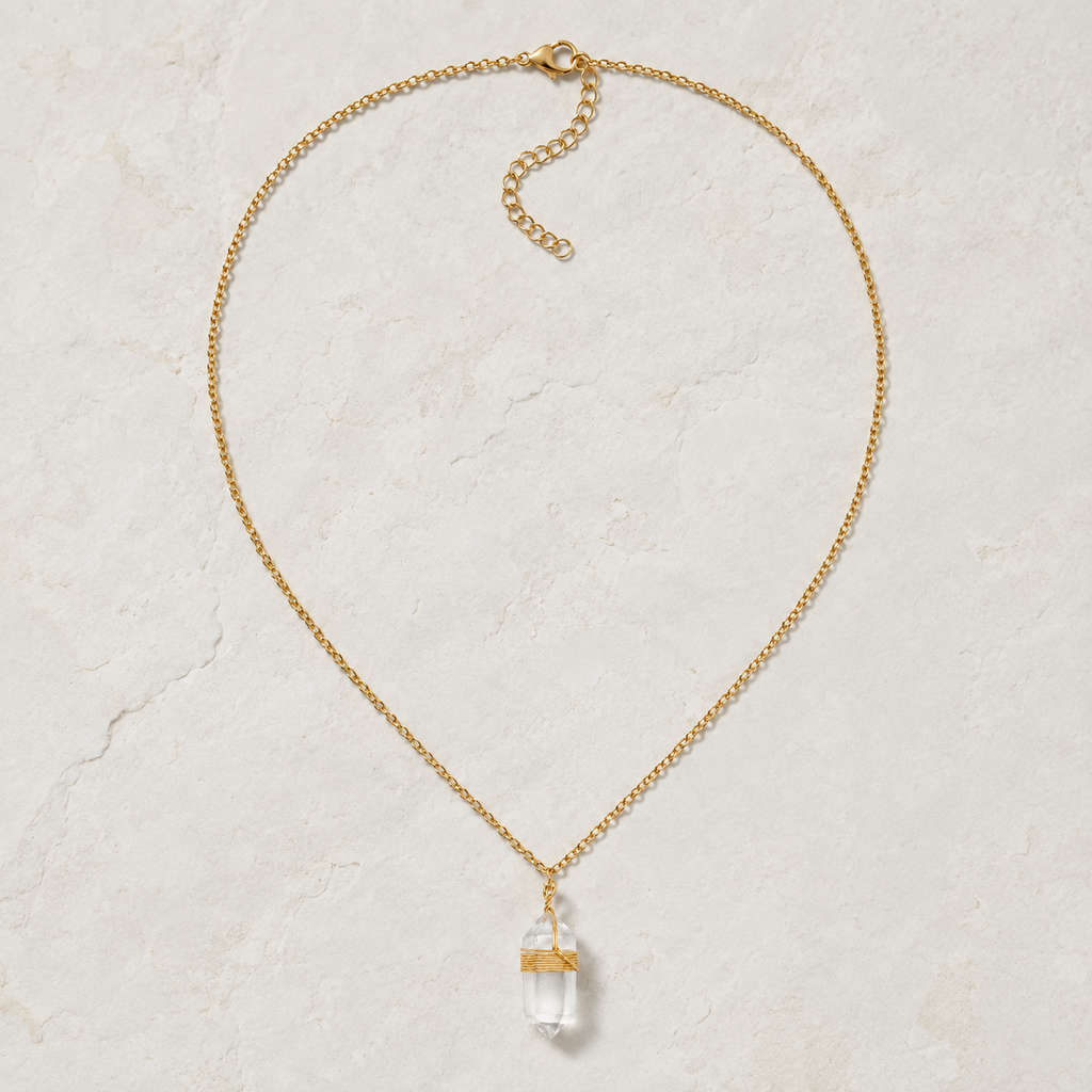 Collier doré en cristal de roche présenté en entier sur une surface minérale claire