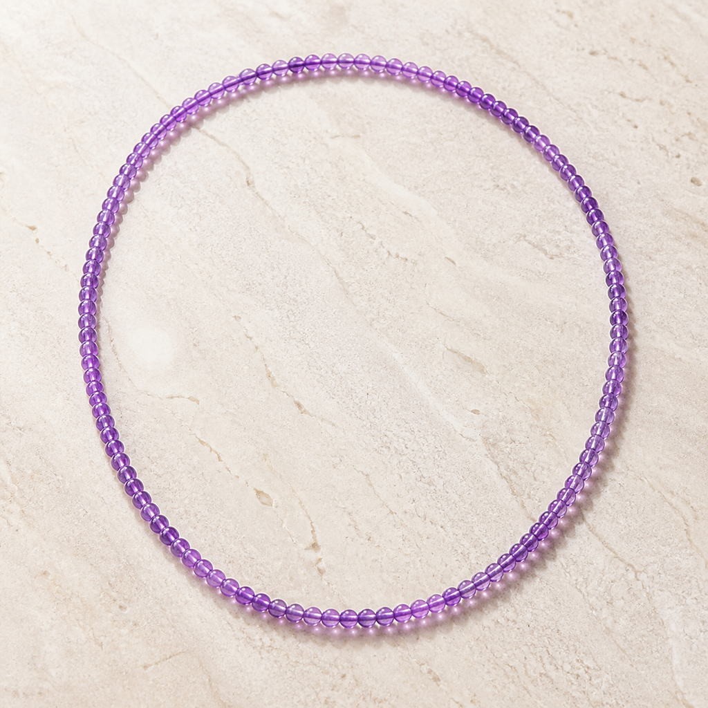 Collier en améthyste du Brésil 4 mm - 45 cm, vue complète sur une surface minérale claire