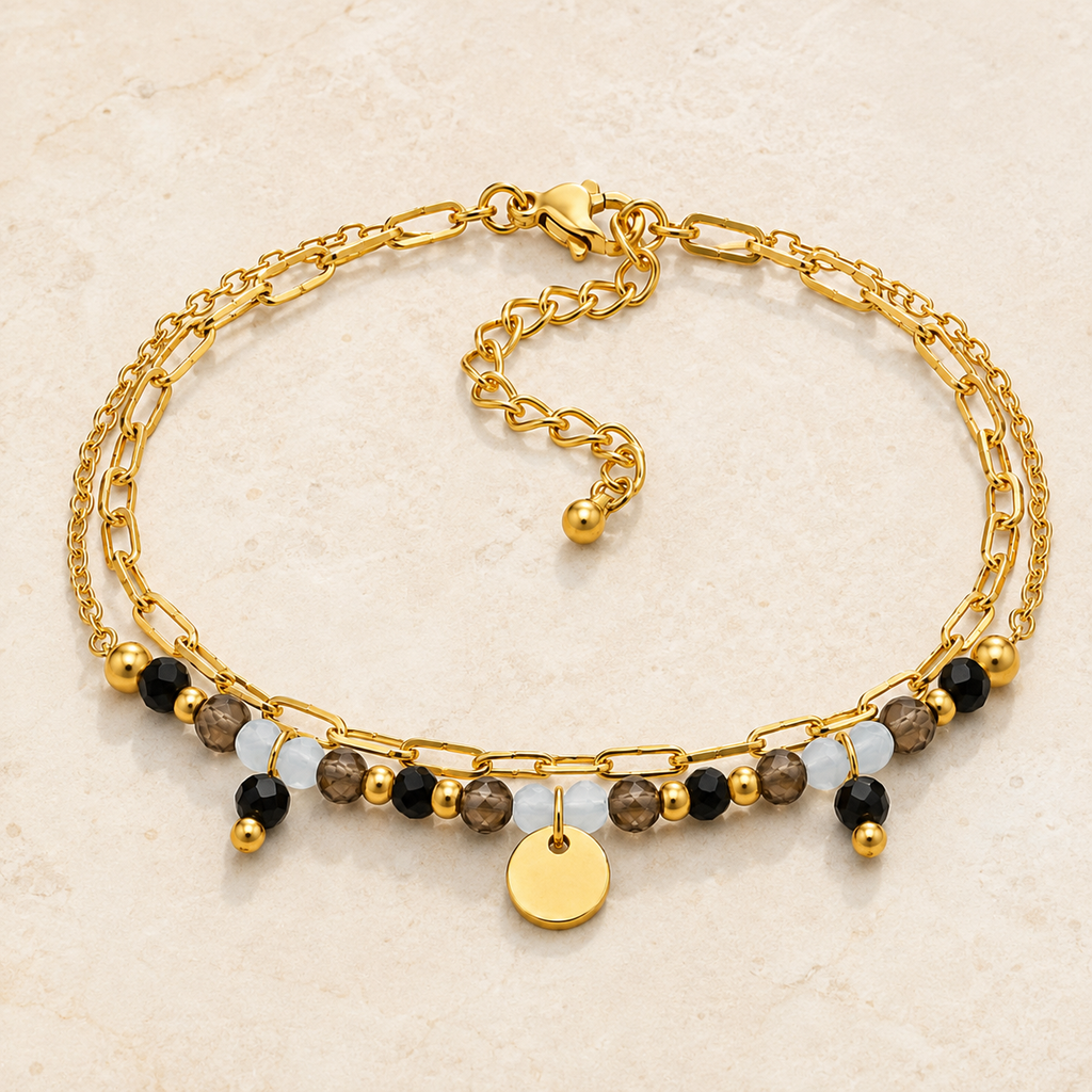 Bracelet doré en tourmaline, quartz fumé et aigue-marine présenté en entier sur une surface minérale claire
