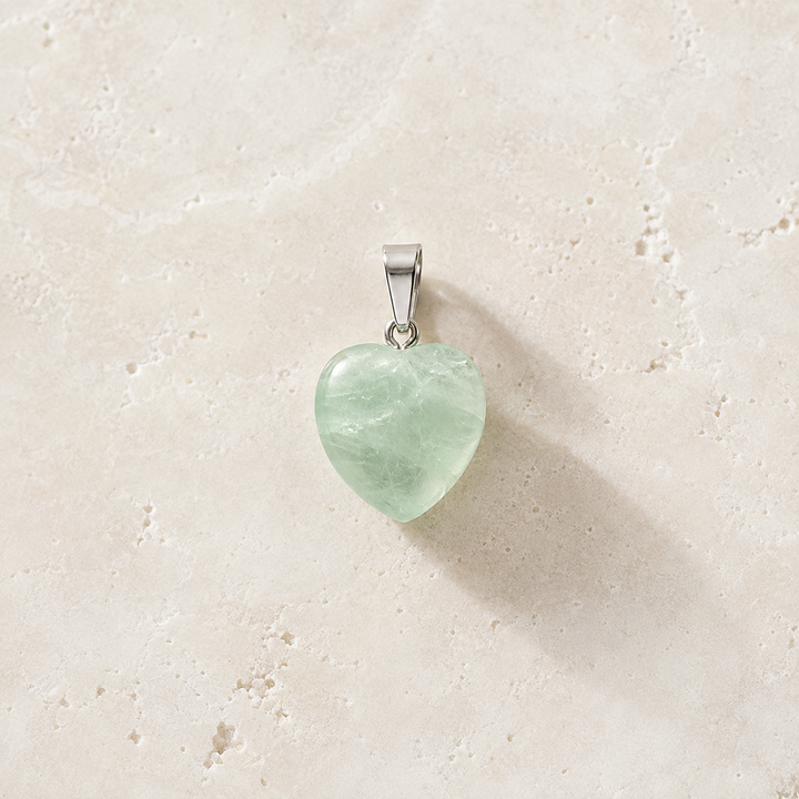 Pendentif cœur en fluorine verte avec sa bélière argentée sur pierre claire