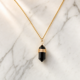Collier boho doré avec pierre d’obsidienne noire sur fond marbre clair