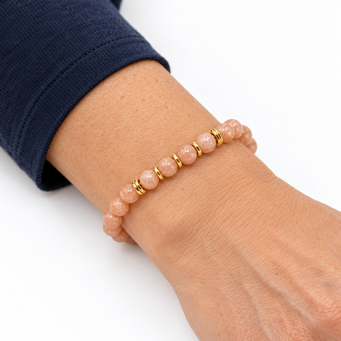 Bracelet en pierre de lune rose porté sur un poignet incliné, perles pêche et séparateurs dorés