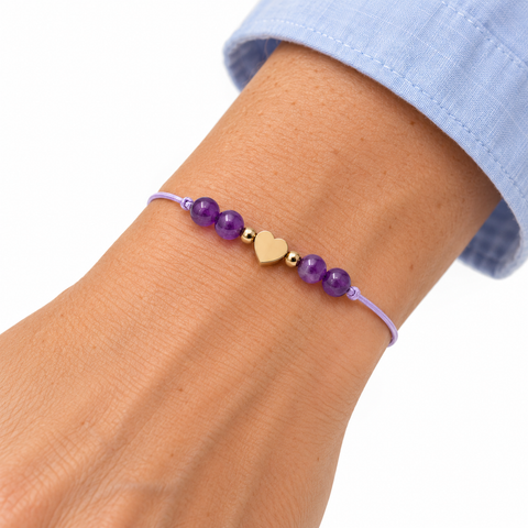 Bracelet cœur doré et quatre améthystes porté sur un poignet incliné, manche bleu clair