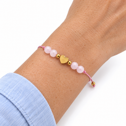 Bracelet cœur doré et quatre quartz roses porté sur un poignet incliné, manche bleu clair