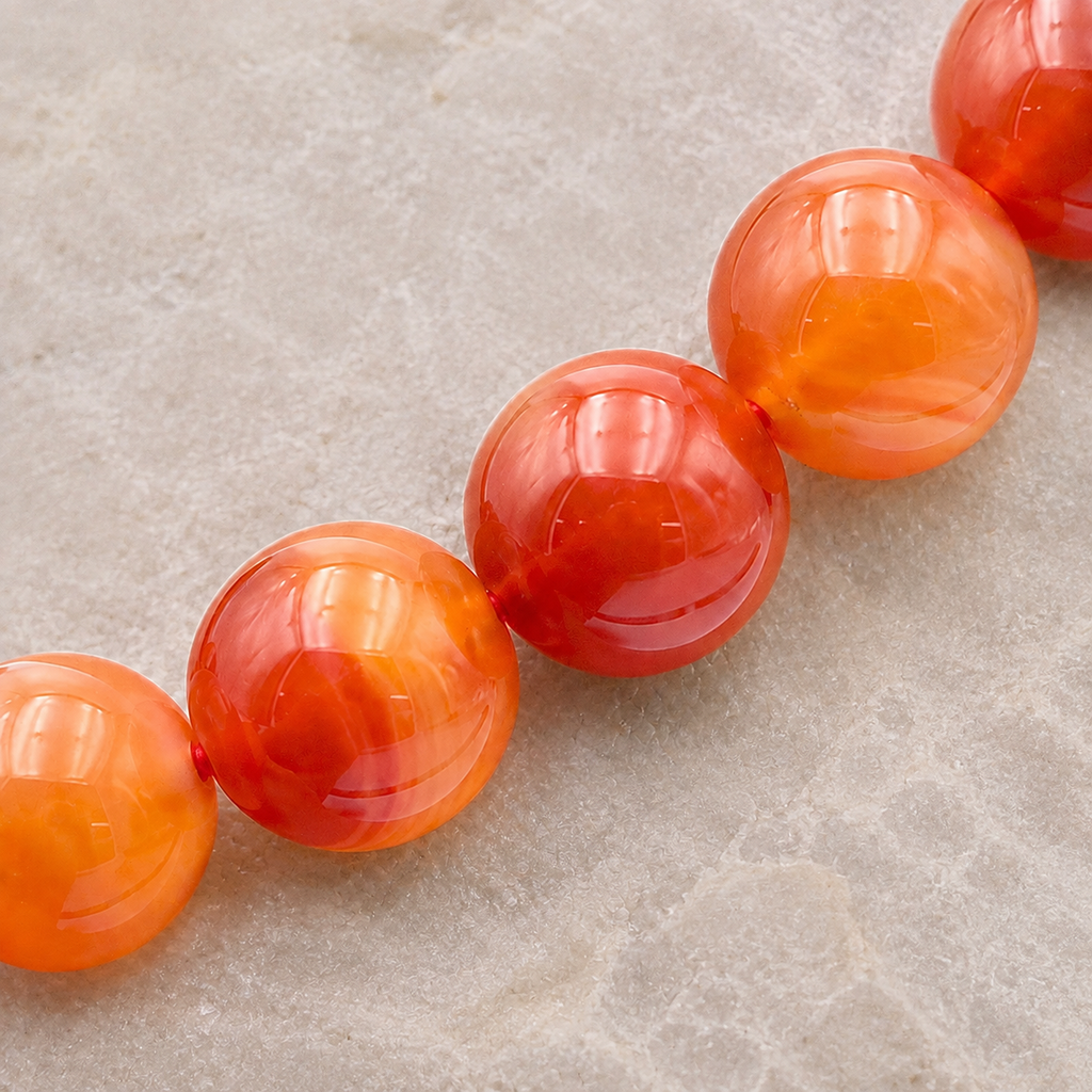 Détail des perles de cornaline orange et rouge et de leur fil élastique