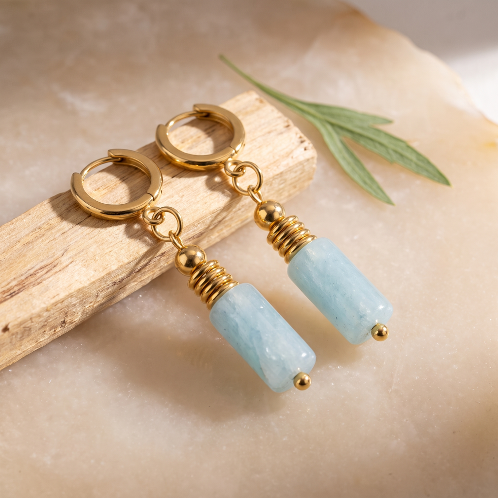 Boucles d'oreilles en aigue-marine dans une nature morte minérale avec feuillage discret