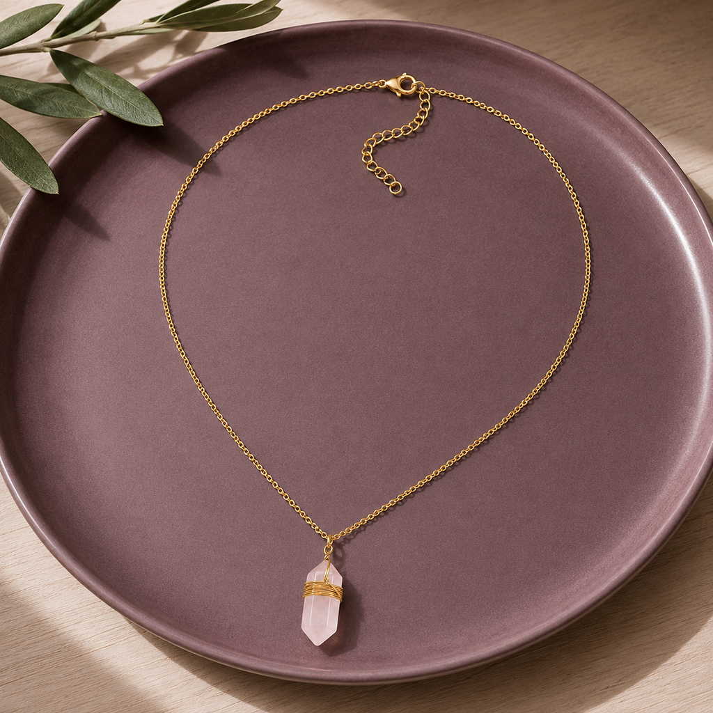 Collier doré en quartz rose en nature morte près d’un feuillage