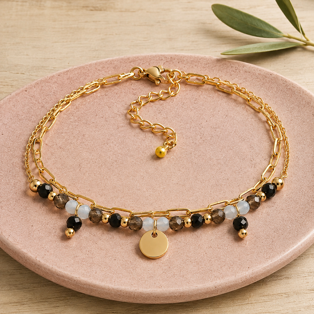 Bracelet doré en tourmaline, quartz fumé et aigue-marine en nature morte près d’un feuillage
