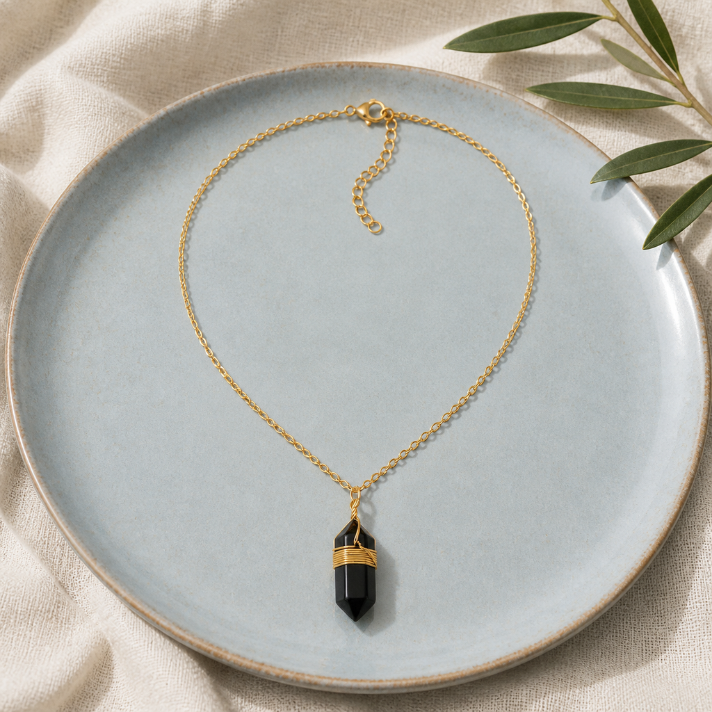 Collier doré en obsidienne noire en nature morte près d’un feuillage