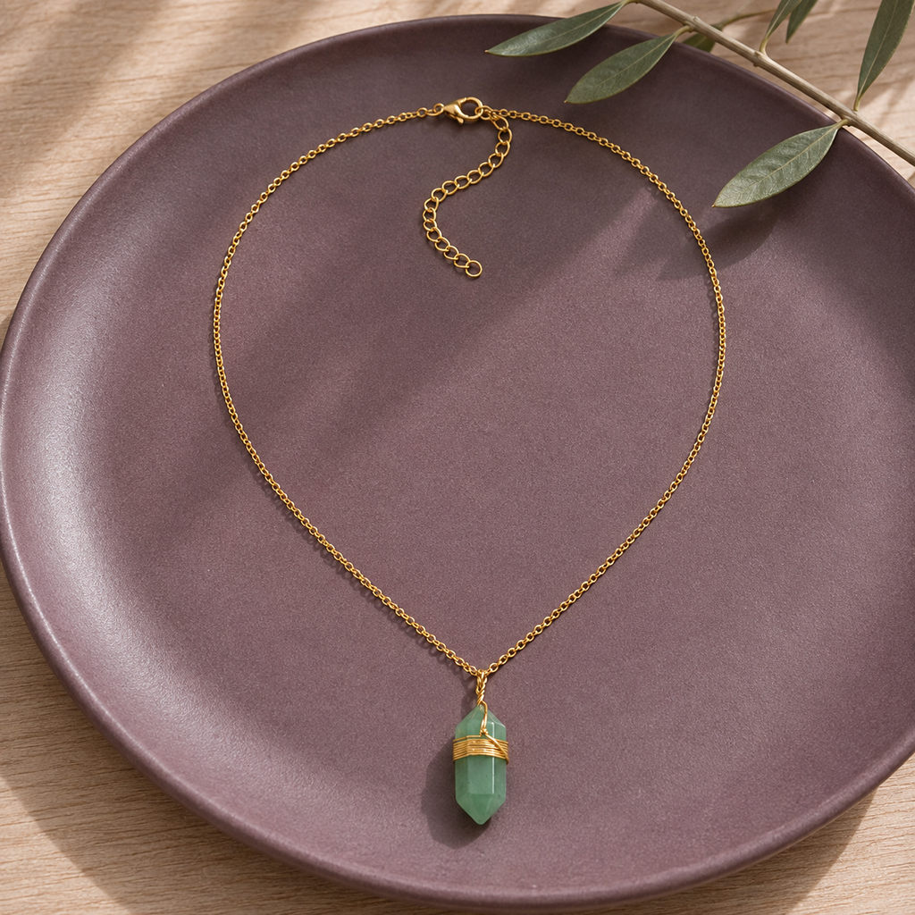 Collier doré en aventurine verte en nature morte près d’un feuillage