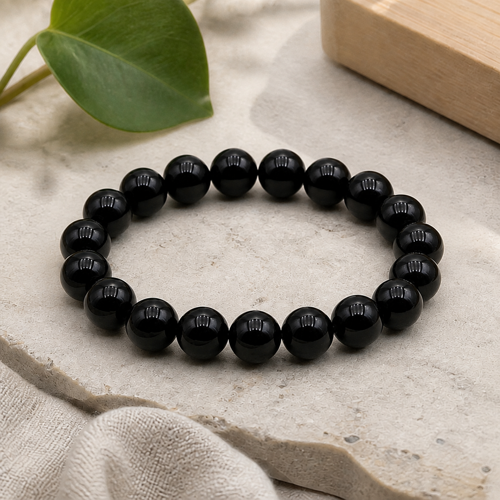 Bracelet en obsidienne noire posé sur une pierre claire près d’une feuille verte