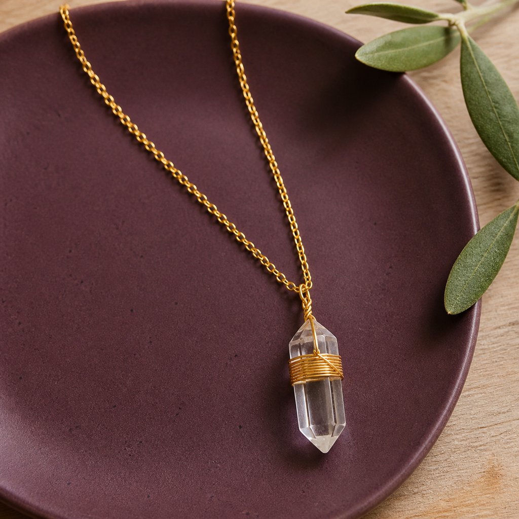 Collier doré en cristal de roche en nature morte près d’un feuillage