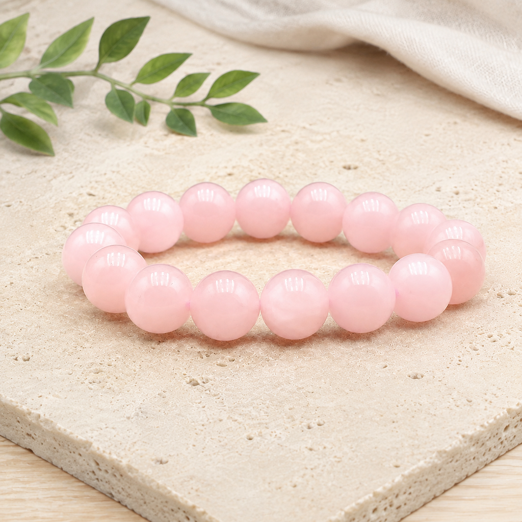 Bracelet en quartz rose sur une plaque minérale claire avec du lin et une branche verte