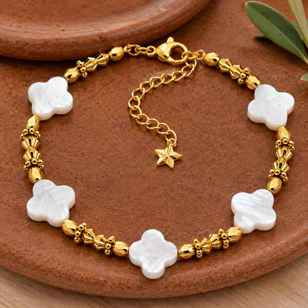 Bracelet doré à fleurs de nacre en nature morte près d’un feuillage