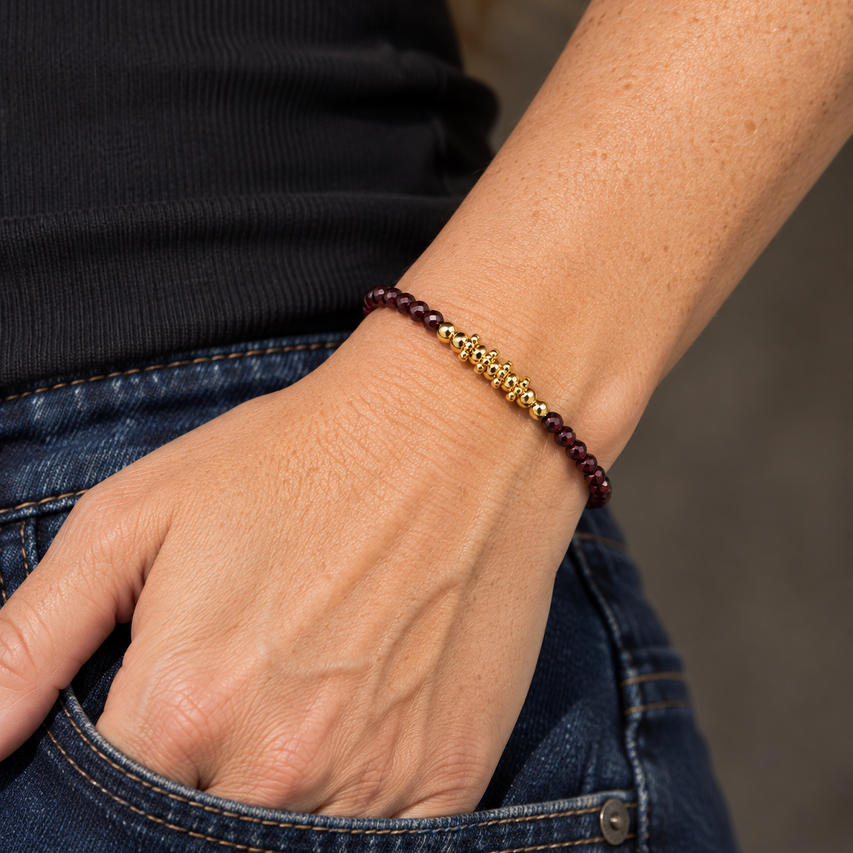 Bracelet doré en grenat rhodolite porté au poignet près d'une poche en denim sombre