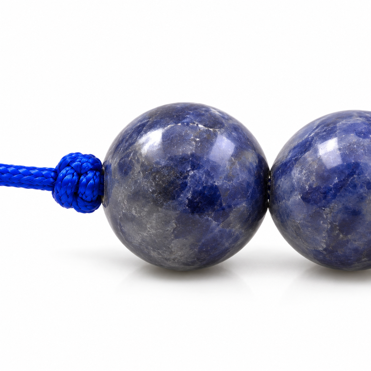 Détail d’une perle de sodalite polie, nuances bleues et zones grises naturelles