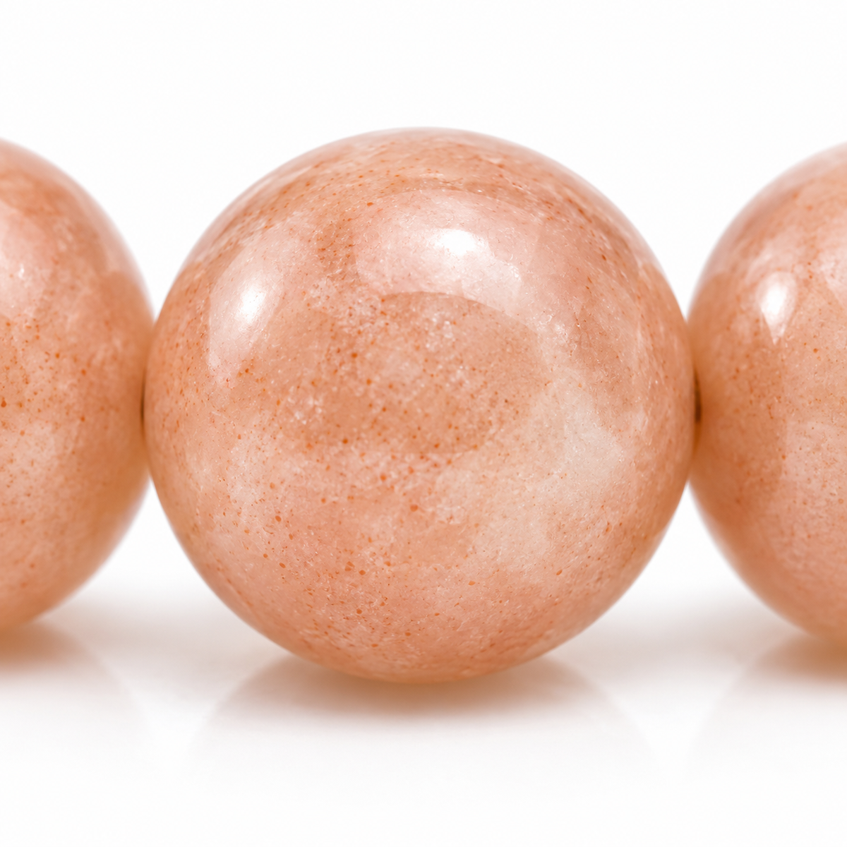 Gros plan d’une perle polie en pierre de lune rose, nuances pêche et variations internes