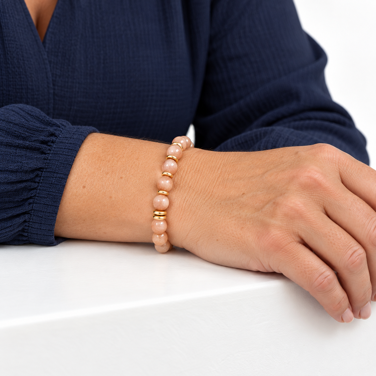 Bracelet en pierre de lune rose porté, avant-bras posé sur une surface blanche